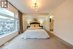Spacious room featuring floor-to-ceiling windows, light-toned carpeting, a contemporary ceiling light fixture, and an entrance to an adjoining bathroom with a vanity - 