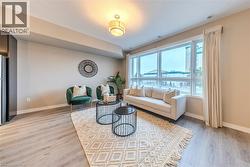 Expansive living area featuring a large window wall with roller blinds, wood-finish flooring, and a contemporary ceiling light fixture - 