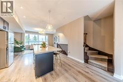 Open-concept living area featuring wood-finish flooring throughout, a central kitchen island with a stone countertop, and a contemporary pendant lighting fixture - 