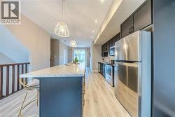 Modern kitchen featuring an extended island with a light-toned countertop, dark cabinetry, stainless steel appliances, contemporary pendant lighting, and wood-finish flooring - 