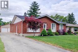 Brick exterior residence with a gabled roofline, featuring a paved driveway, an attached garage, and a detached auxiliary structure with a garage door - 