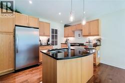 Kitchen featuring wood-finish cabinetry, black countertops, and a stainless steel refrigerator - 