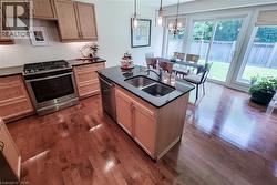Kitchen featuring a central island with an undermount double-basin sink, black countertops, and light wood cabinetry - 