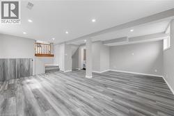 Spacious room featuring light grey walls, grey wood-style flooring, recessed lighting, and a white-framed window - 