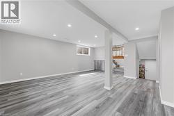 Spacious room featuring light grey walls, grey wood-style flooring, recessed lighting, and a visible window - 