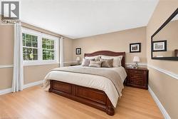 Bedroom with light wood-finish flooring, a large window, neutral wall paint, white trim, and crown molding - 