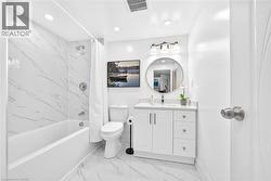 Bathroom featuring white marble-look wall and floor tile, a white vanity with a light-colored countertop, and a circular mirror with an overhead three-light fixture - 