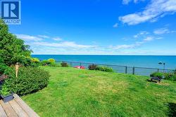 Manicured lawn leading to expansive water frontage, bordered by lush landscaping and mature trees - 