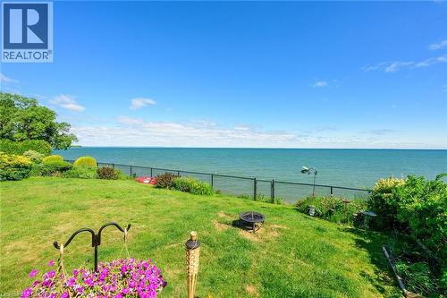 Grassed backyard with mature landscaping and a black chain-link fence bordering the water - 15 Cheval Drive, Grimsby, ON - Outdoor With Body Of Water With View