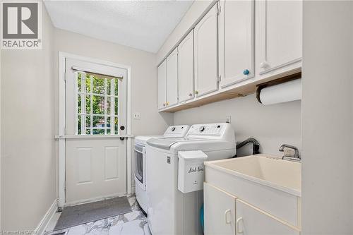 Dedicated laundry room featuring white cabinetry, a utility sink, and durable marble-look flooring - 15 Cheval Drive, Grimsby, ON - Indoor Photo Showing Laundry Room