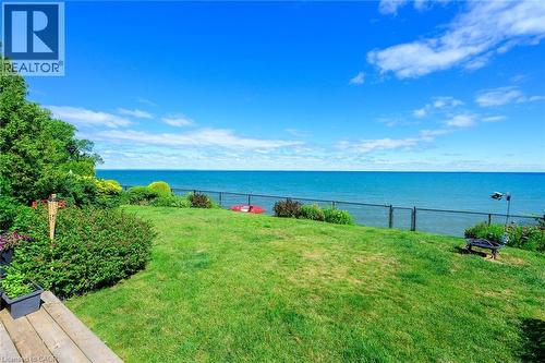 Manicured lawn leading to expansive water frontage, bordered by lush landscaping and mature trees - 15 Cheval Drive, Grimsby, ON - Outdoor With Body Of Water With View