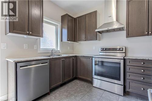 Contemporary kitchen featuring dark wood-finish cabinetry, light-toned countertops, a stainless steel dishwasher, a stainless steel range with a coordinating hood vent, and tile flooring - 3896 Tufgar Crescent, Burlington, ON 