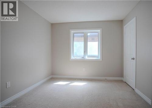 Carpeted room featuring a white-framed window, neutral painted walls, white trim, and a white paneled door with a silver-toned knob - 3896 Tufgar Crescent, Burlington, ON 