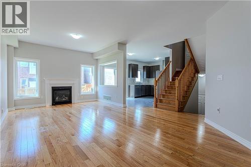 Open-concept living area featuring wood-finish flooring, a contemporary fireplace with a classic mantel, and multiple windows - 3896 Tufgar Crescent, Burlington, ON 