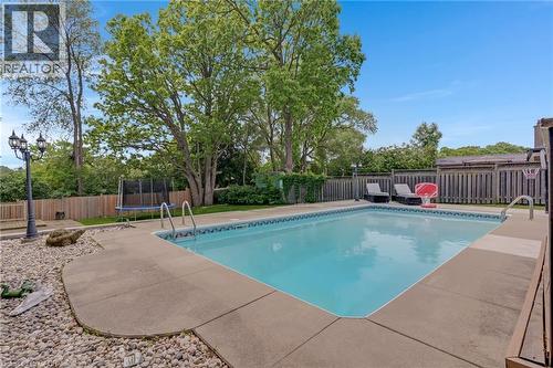 In-ground swimming pool with concrete surround, bordered by a wooden fence and mature trees - 139 Dorset Road, Cambridge, ON 
