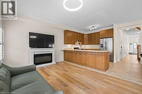 Open-concept living area with light wood-finish flooring, a contemporary fireplace with a white mantel, and a kitchen featuring wood cabinetry, light countertops, and stainless steel appliances - 4670 Thomas Alton Boulevard, Burlington, ON 