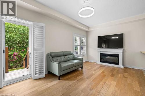Living area featuring wood-finish flooring, a contemporary fireplace with a white mantel, and a sliding glass door leading to a wooden deck - 4670 Thomas Alton Boulevard, Burlington, ON 