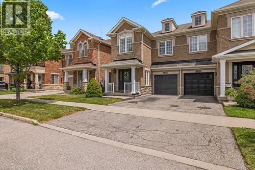 Brick facade townhouse featuring a covered front porch with white railings, two attached garage doors, and dormer windows - 4670 Thomas Alton Boulevard, Burlington, ON 