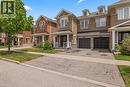 Brick facade townhouse featuring a covered front porch with white railings, two attached garage doors, and dormer windows - 4670 Thomas Alton Boulevard, Burlington, ON 