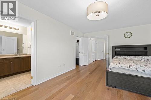 Bedroom featuring wood-finish flooring, a contemporary drum light fixture, and an open doorway revealing an attached bathroom - 4670 Thomas Alton Boulevard, Burlington, ON 