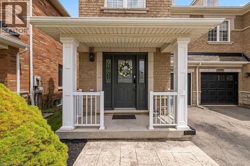 Covered front porch with white columns and railings, featuring a dark gray door with decorative glass inserts - 4670 Thomas Alton Boulevard, Burlington, ON 