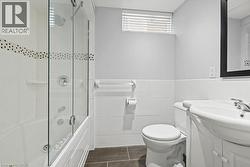 Bathroom featuring a jetted tub with glass shower enclosure, white tile surround with decorative accent, a pedestal vanity, and dark tile flooring - 