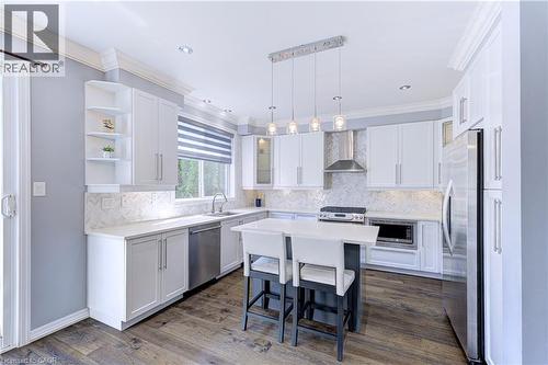 Contemporary kitchen featuring a central island with countertop seating, stainless steel appliances, white cabinetry with crown molding, a patterned tile backsplash, and wood-finish flooring - 1406 Marshall Crescent, Milton, ON 