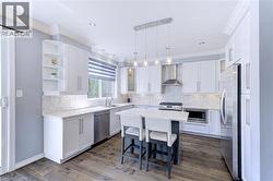 Contemporary kitchen featuring a central island with countertop seating, stainless steel appliances, white cabinetry with crown molding, a patterned tile backsplash, and wood-finish flooring - 