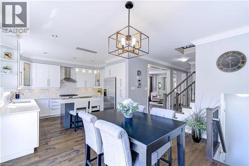 Open-concept kitchen and dining area featuring white shaker cabinetry, stainless steel appliances, wood-finish flooring, a central island with seating, and a geometric pendant light fixture - 1406 Marshall Crescent, Milton, ON 