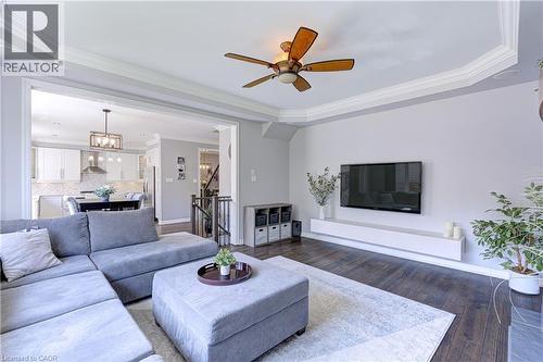 Living space featuring dark wood-finish flooring, a tray ceiling with crown molding, and a ceiling fan - 1406 Marshall Crescent, Milton, ON 