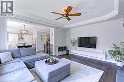 Living space featuring dark wood-finish flooring, a tray ceiling with crown molding, and a ceiling fan - 