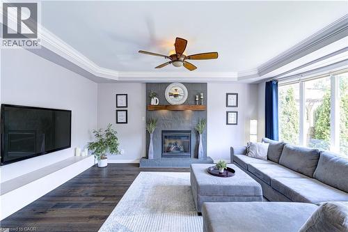 Living area featuring a stone-clad fireplace with a wood mantel, crown molding, wood-finish flooring, a ceiling fan, and large windows - 1406 Marshall Crescent, Milton, ON 
