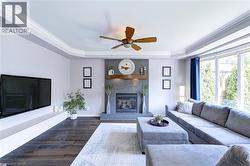 Living area featuring a stone-clad fireplace with a wood mantel, crown molding, wood-finish flooring, a ceiling fan, and large windows - 