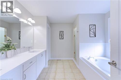 Bathroom featuring a dual vanity with white cabinetry and integrated sinks, a built-in bathtub with white tile surround, and tile flooring - 1406 Marshall Crescent, Milton, ON 