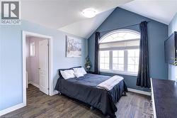 Vaulted ceiling bedroom featuring a large arched window with horizontal blinds and dark drapery - 