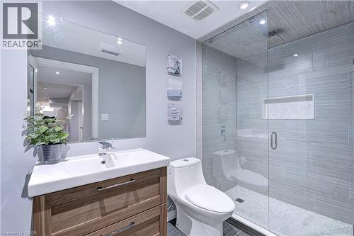 Bathroom featuring a wood-finish vanity with an integrated white sink, a frameless wall mirror, and a glass-enclosed shower with horizontal tile walls - 1406 Marshall Crescent, Milton, ON 