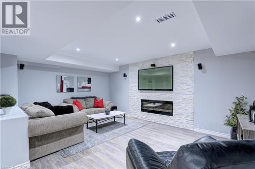 Living area featuring wood-finish flooring, a stacked stone accent wall, and a built-in linear fireplace - 1406 Marshall Crescent, Milton, ON 
