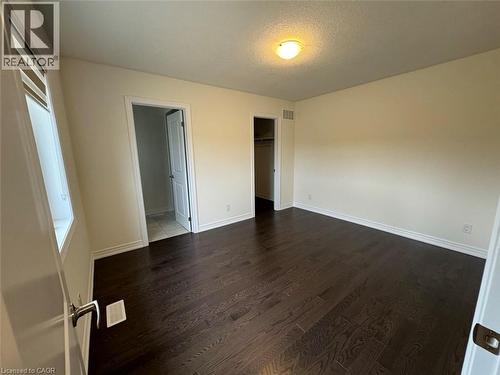 Spacious room featuring dark wood-finish flooring, light neutral-toned walls, and white baseboards - 10 Guernsey Drive Unit# Upper, Kitchener, ON 