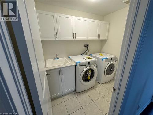Laundry area featuring white shaker-style cabinetry, a utility sink, and light-toned tile flooring - 10 Guernsey Drive Unit# Upper, Kitchener, ON 