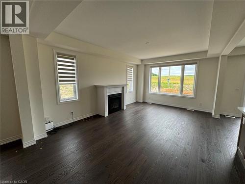 Spacious living area featuring dark wood-finish flooring, a contemporary electric fireplace with a white mantel, and large windows providing ample natural light - 10 Guernsey Drive Unit# Upper, Kitchener, ON 