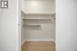 Spacious walk-in closet featuring light wood-finish flooring, white baseboards, and built-in adjustable shelving systems - 