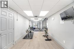 Fitness area featuring wood-finish flooring, drop ceiling with integrated lighting, wall-mounted television, and glass-paneled doors - 