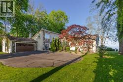Stone and stucco exterior featuring a two-car garage with a paneled door, mature landscaping, and a paved driveway - 
