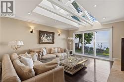 Living area with wood-finish flooring, a vaulted ceiling with exposed beams and skylights, and recessed lighting - 