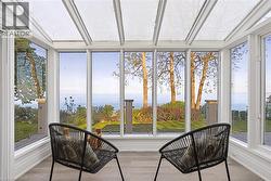 Sunroom featuring a full glass roof, expansive windows framing an ocean backdrop, wood-finish flooring, and white trim - 