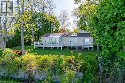 Rear exterior featuring a large deck with glass panel railings, a sunroom with a glass roof, and multiple skylights - 