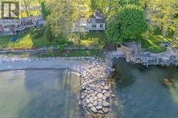 Waterfront property featuring a private pebble beach, extensive rock breakwater, multi-level wooden deck with stairs, and mature trees - 