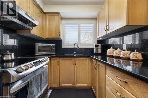 Kitchen featuring wood cabinetry, black countertops, a stainless steel range, and a window with plantation shutters - 125 Terni Boulevard, Hamilton, ON 