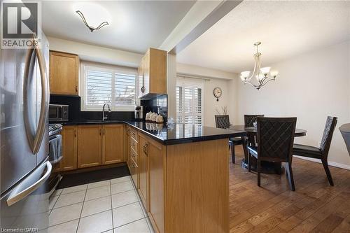 Open-concept kitchen and dining area featuring natural wood cabinetry, dark countertops, white tile flooring in the kitchen, and wood-finish flooring in the dining area - 125 Terni Boulevard, Hamilton, ON 