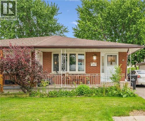 Brick exterior featuring a covered front porch with white railings, a brown asphalt shingle roof, and a mature red-leafed shrub - 35 Vicmount Drive, Kitchener, ON 